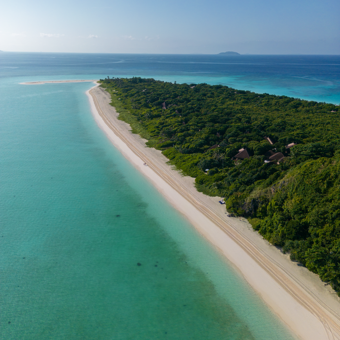 Aerial view of Amanpulo's eastern shore beach, with white sand meeting turquoise waters and dense tropical vegetation.