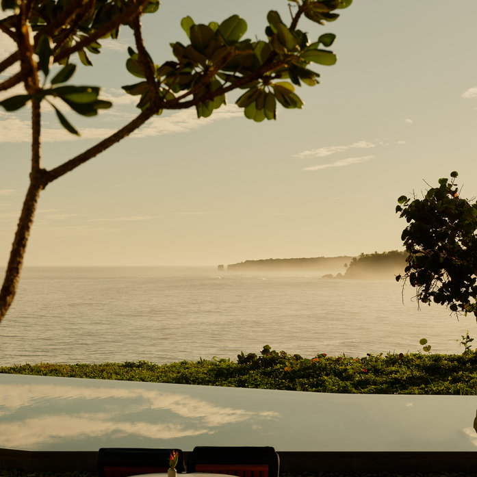 Amanera's pool overlooking coastal landscape at dusk, with curved loungers in foreground.