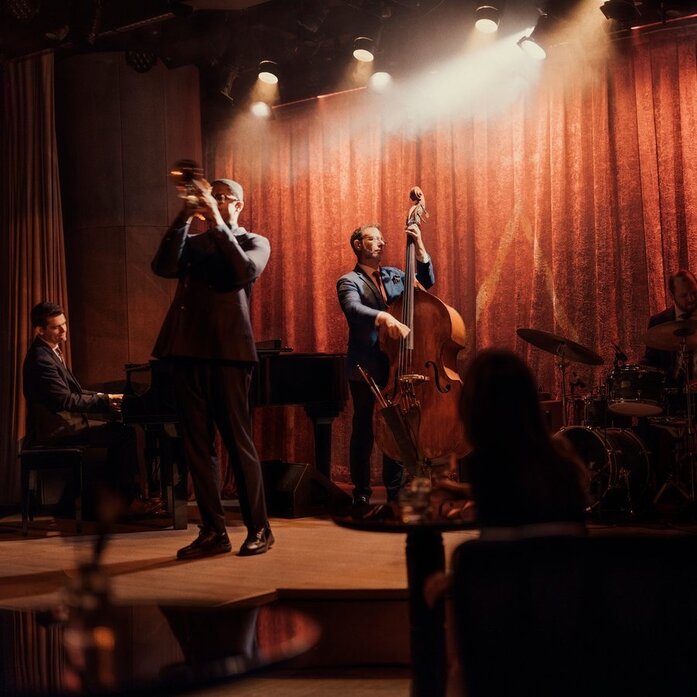 Jazz band performing on stage at Aman New York's intimate jazz club, with warm lighting and red curtains.