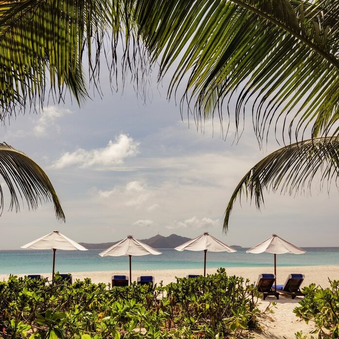 Picnic Grove at Amanpulo with beach umbrellas, palm fronds, and turquoise waters of the Philippine archipelago beyond.
