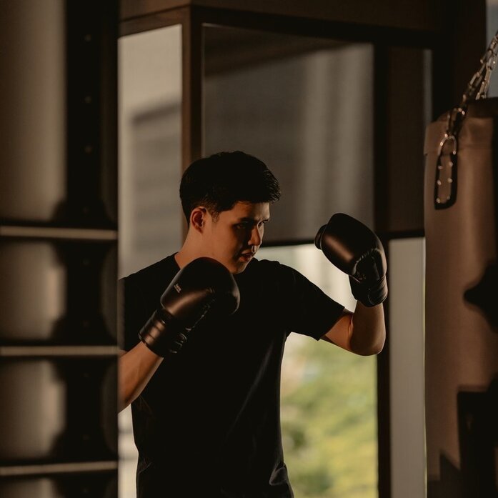 Boxer training at Aman Nai Lert Bangkok's gym, practising Thai boxing techniques on a heavy bag.