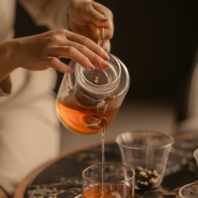 Hands pouring tea into a glass at Aman Nai Lert Bangkok, Thailand.