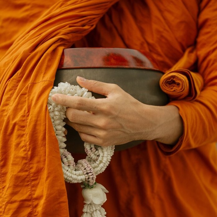 Buddhist monk in saffron robes holding a book and jasmine garlands at Aman Nai Lert Bangkok, Thailand.