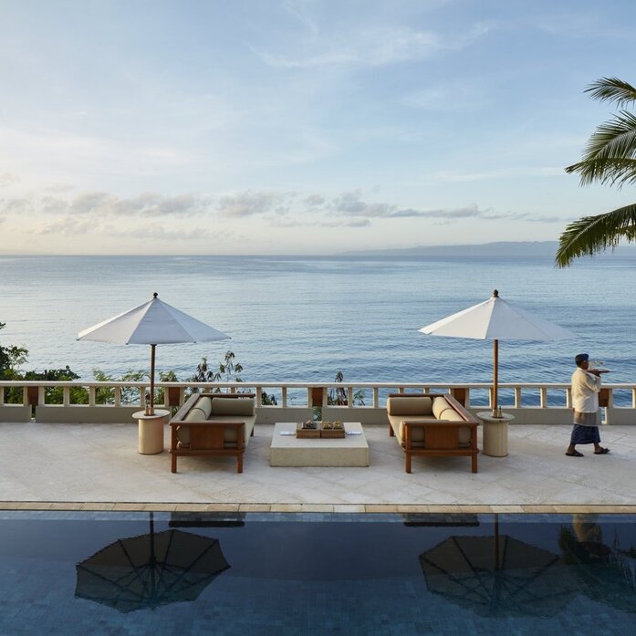 Amankila Suite terrace with seafront views, umbrellas, and seating areas overlooking calm waters in Indonesia.