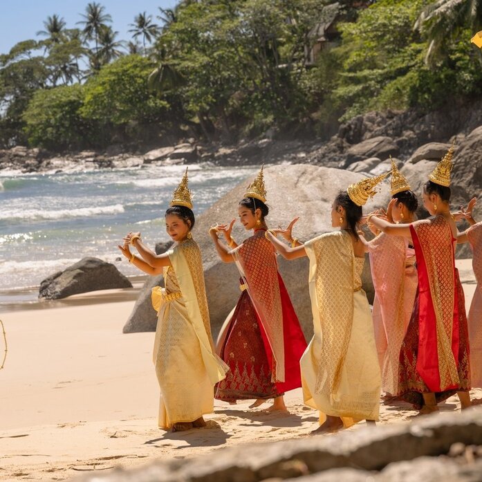Buddhist monks in saffron and orange robes gathered on a sandy beach at Amanpuri during Songkran celebrations.