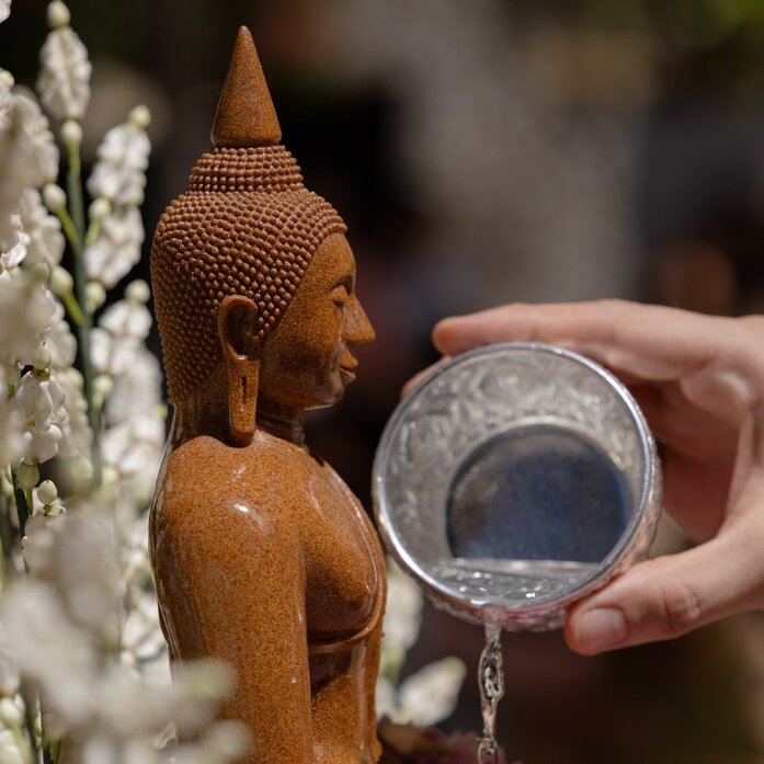 Buddhist monk pouring water over wooden Buddha statue during Songkran celebration at Amanpuri, Thailand.