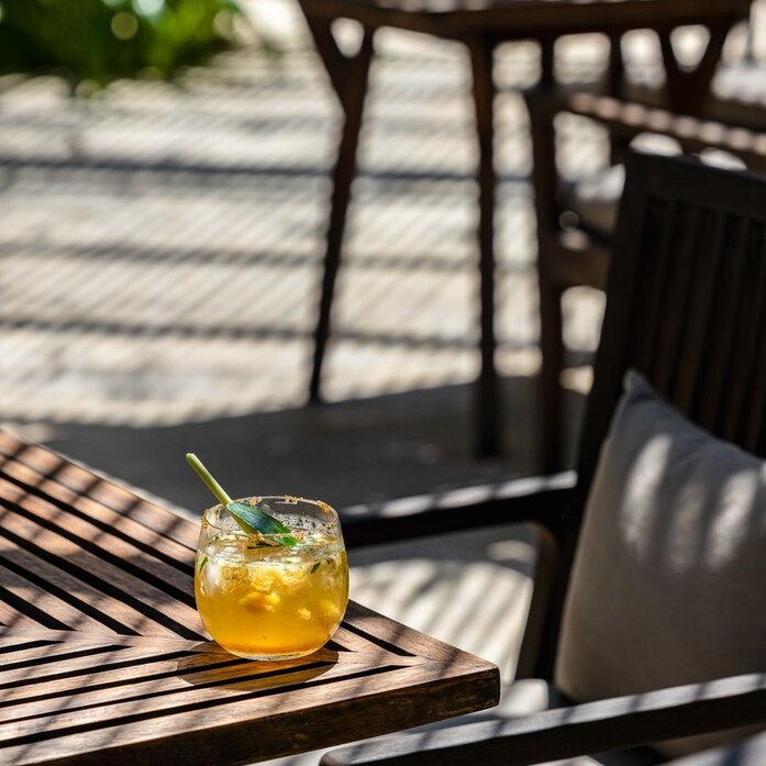 Apsara Crush cocktail on a wooden table at Amansara, Cambodia, with dappled sunlight.