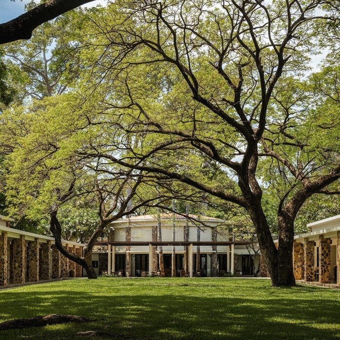 Amansara garden suite corridor framed by mature tree canopy and manicured lawn.