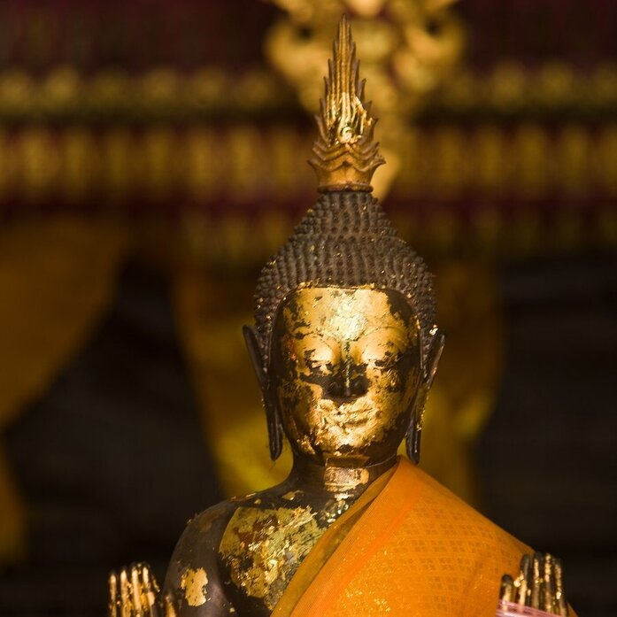 Golden Buddha statue draped in saffron robes at Amantaka's temple in Luang Prabang.