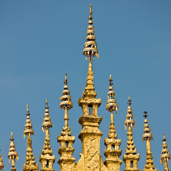 Gilded temple spires with ornate details against clear blue sky at Amantaka, Luang Prabang.