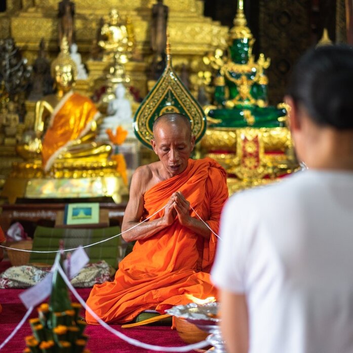 Monk in saffron robes seated before gilded Buddha statues at Amantaka, Luang Prabang.