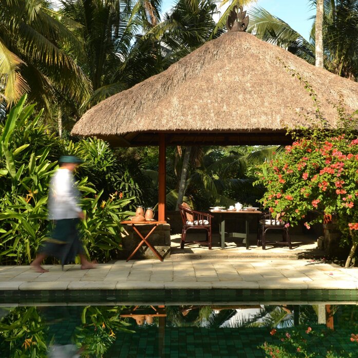 Thatched-roof pool villa at Amandari with stone platform, framed by tropical vegetation and clear sky.