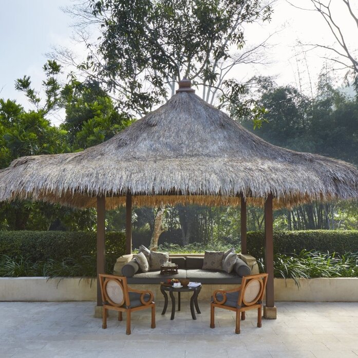 Garden pavilion with thatched roof at Amanjiwo, featuring wooden seating beneath.