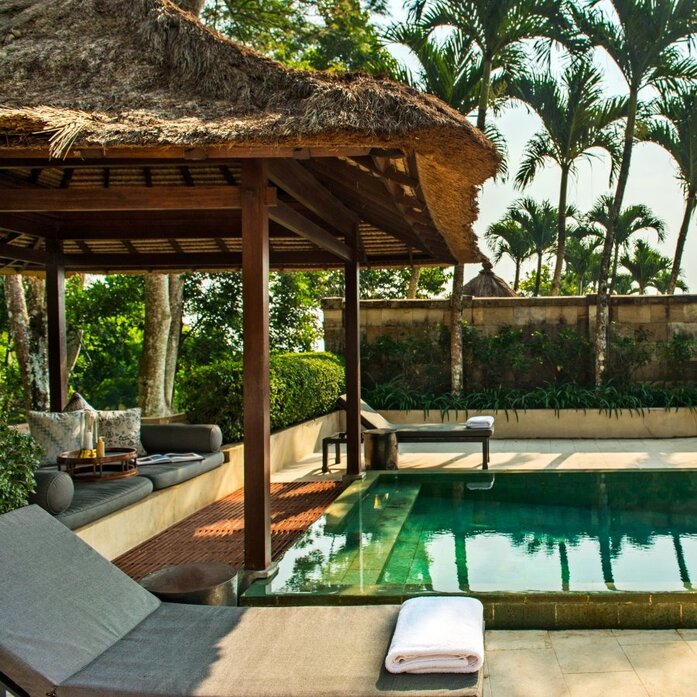 Garden pool pavilion at Amanjiwo with shaded seating area overlooking emerald water, Indonesia.