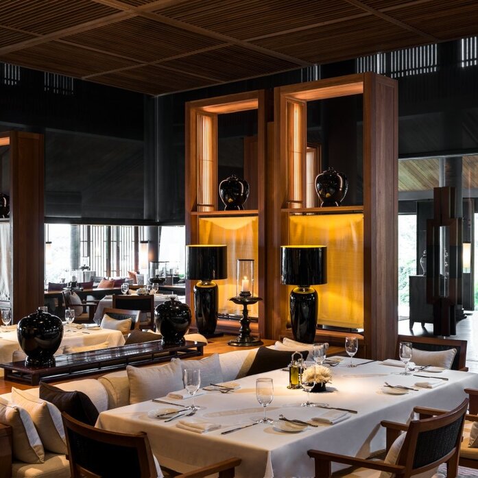 Amanoi's main dining restaurant with warm wooden architecture and floor-to-ceiling windows overlooking the landscape.