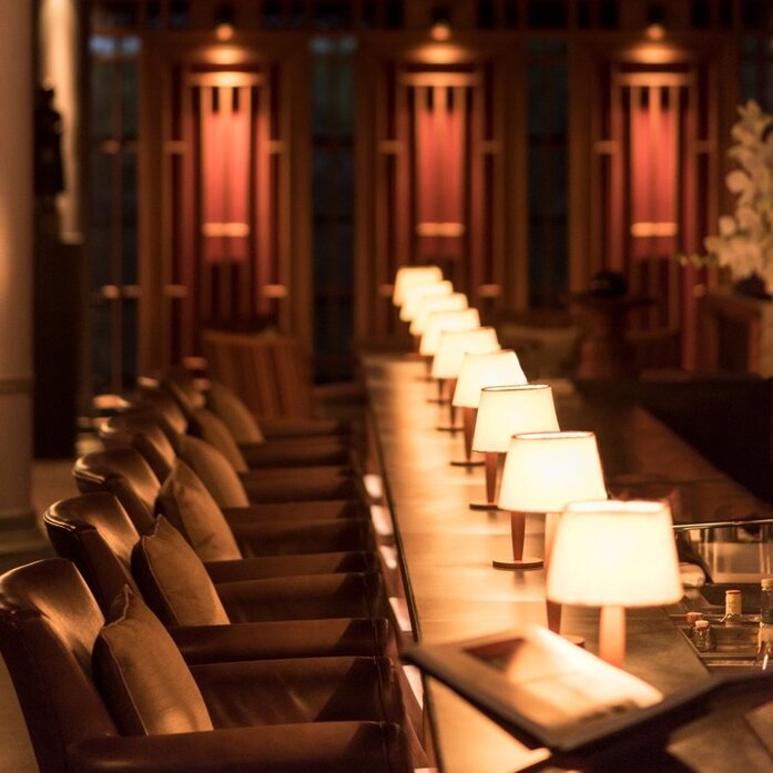 Candlelit dining room at Amanoi with rows of wooden chairs and glowing red wall panels.