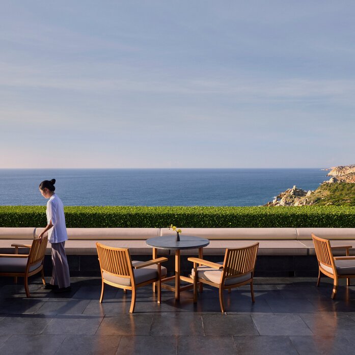 Amanoi's main restaurant terrace overlooking the sea, with wooden dining tables and a solitary figure gazing at the coastline.