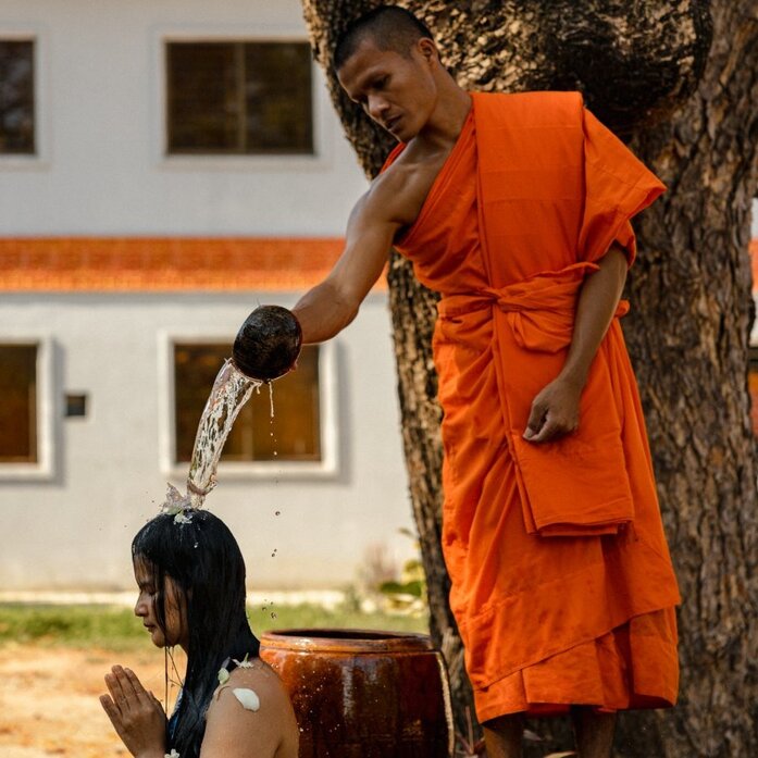 Buddhist monk in saffron robes pouring water over a kneeling guest during a spiritual blessing at Amansara, Cambodia.