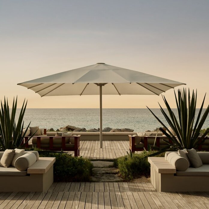 Outdoor living area at Amanyara with grey umbrella, seating and ocean view at dusk.