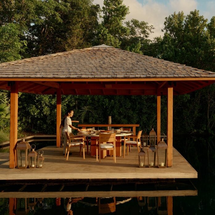 Amanyara villa's private dining pavilion with wooden table and chairs beneath a pitched roof, surrounded by tropical greenery.