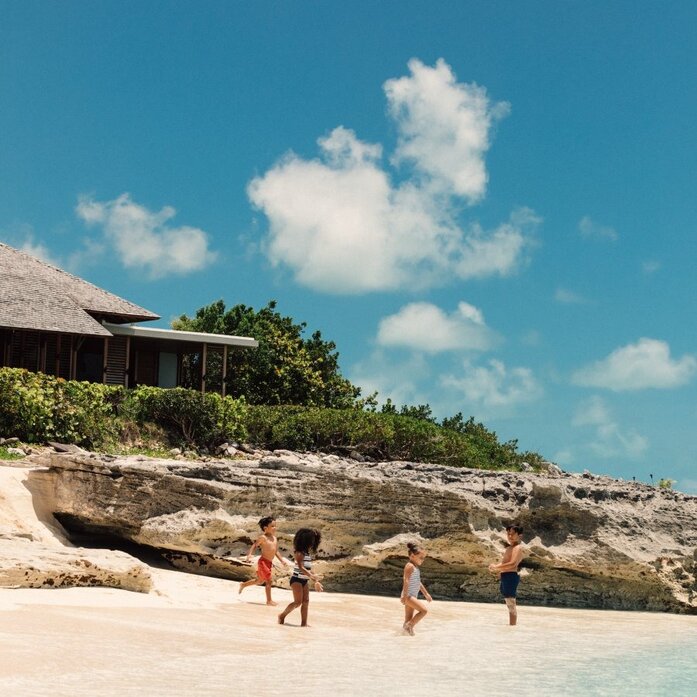 Children playing on a sandy beach beside a rocky cliff at Amanyara, Turks and Caicos.