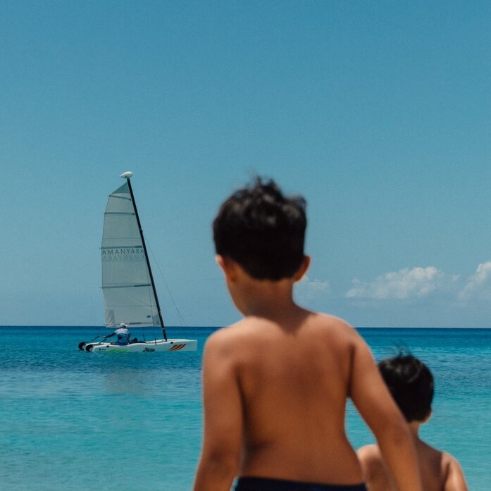 Child watching a sailboat on turquoise waters at Amanyara, Turks and Caicos.