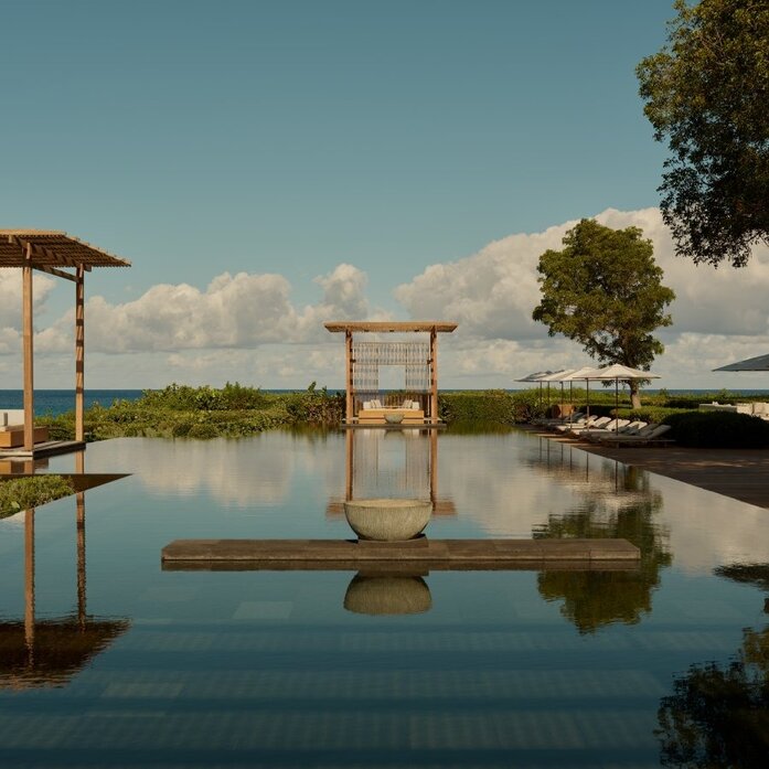 Piscina principal do resort Amanyara em Turks e Caicos, com estruturas de madeira e céu azul ao fundo.