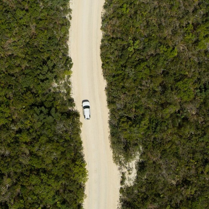 Aerial view of a white sand path through dense green vegetation at Amanyara, Turks and Caicos, with a vehicle approaching.