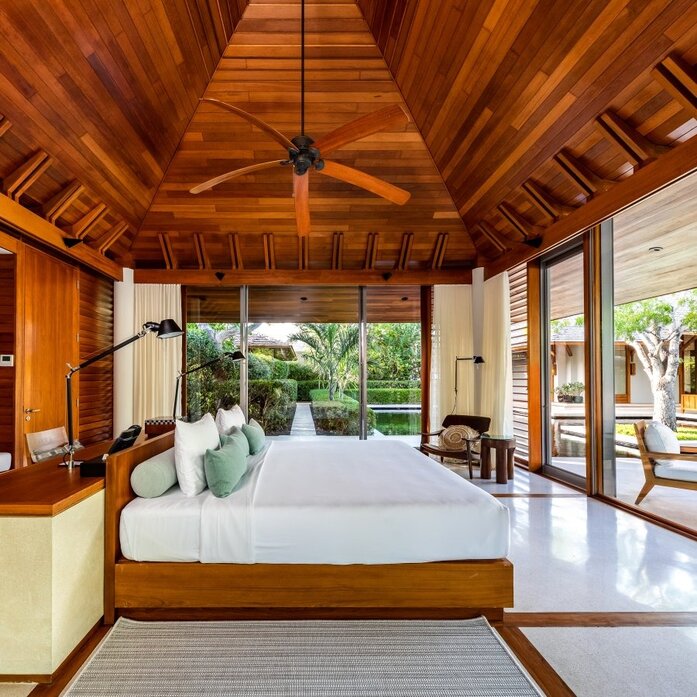 Principal bedroom at Amanyara villa with wooden ceiling, platform bed and garden views through open doors.