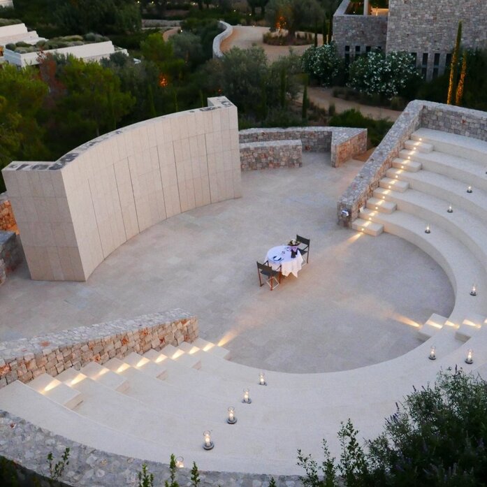 Aerial view of Amanzoe's amphitheatre dining venue in Greece, with curved white architecture and guests seated at tables.