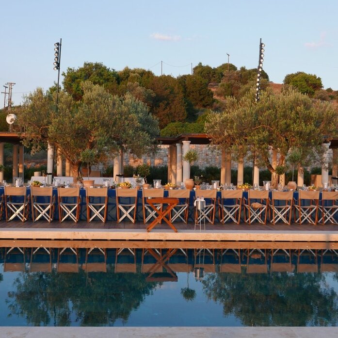 Beach club at Amanzoe with wooden deck overlooking still waters and Mediterranean vegetation.