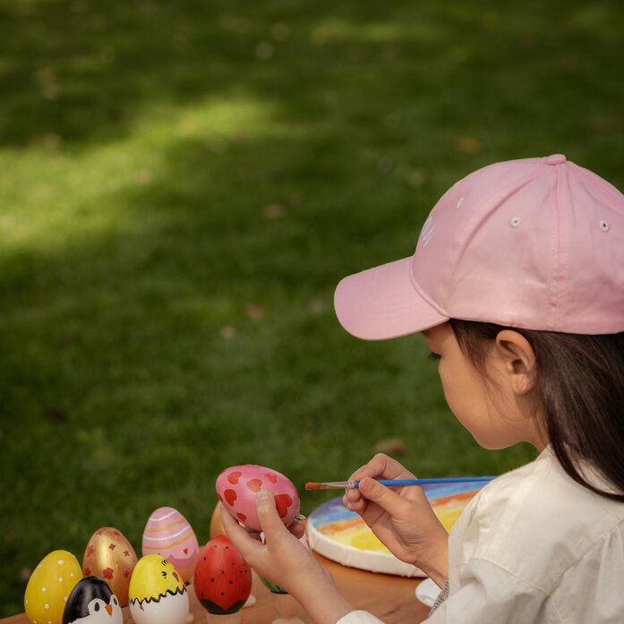 Child in pink cap arranging colourful Easter eggs and crafts outdoors at Amanoi.