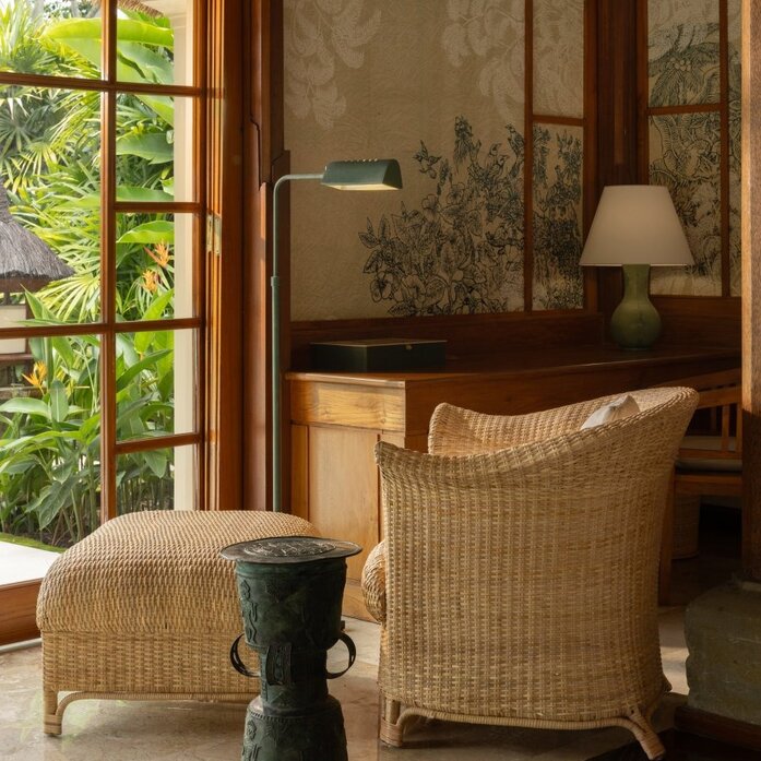 Amandari resort single-story pavilion interior with rattan armchair, natural light from large windows, and lush greenery beyond.
