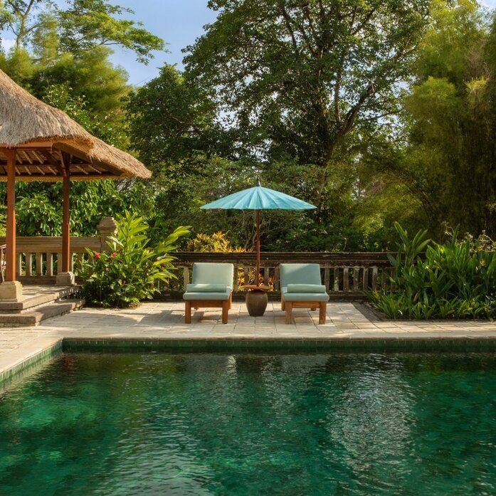 Amandari resort garden pool pavilion dengan sunloungers dan pohon-pohon tropis di sekitarnya.