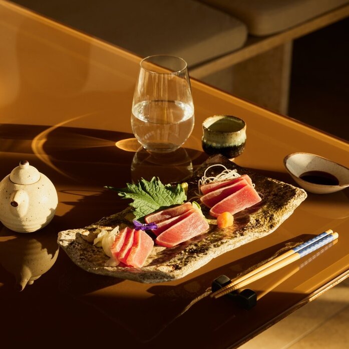 Akari restaurant at Amanzoe serves sashimi and seared fish on a dark plate with warm lighting.