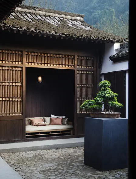 法云安缦度假村的庭院一角，深色木质建筑前放置着白色坐垫，旁边摆放着盆栽树木。