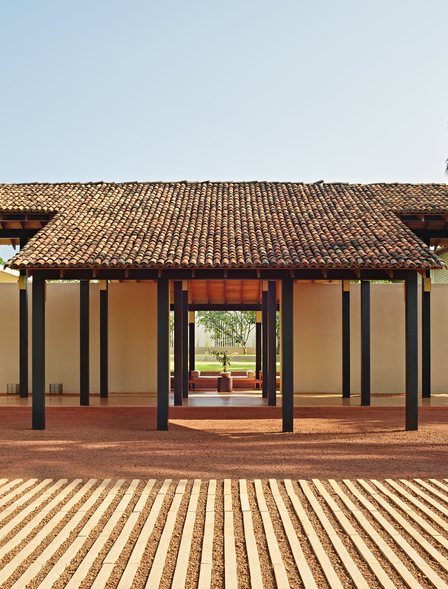 Amanwella's exterior entrance with timber-framed structure and striped wooden decking, flanked by palm trees.