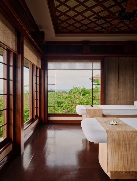 Sala massaggi presso il resort Amanpulo, Filippine, con letto terapeutico e vedute verdi attraverso le finestre.