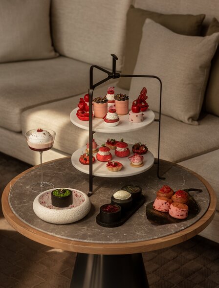 アマン ナイラート バンコクのダイニング会場で、木製テーブルに並べられたアフタヌーンティーセット、ケーキスタンド、デザート、そして照明。