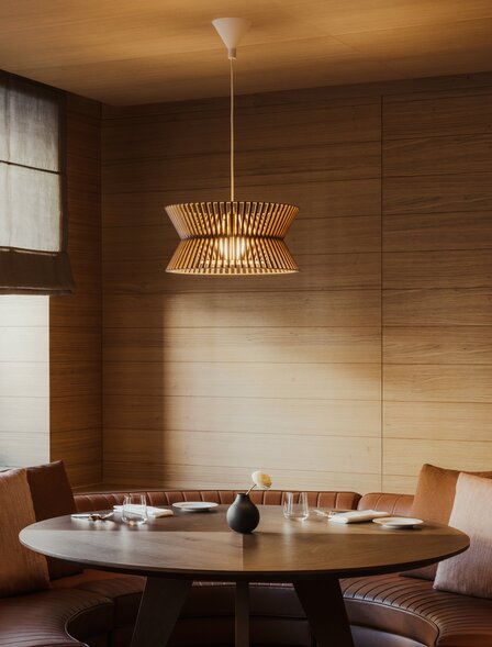 Dining room at Aman Rosa Alpina with round table and brass pendant light, warm wood finishes.