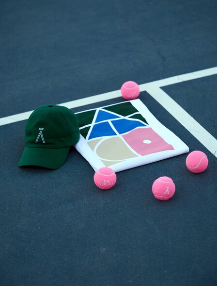 Aman Tennis Club shop display with cap, colourful geometric shapes and pink balls on court surface at Amanzoe.