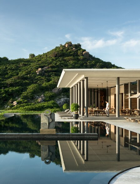 Beach Club at Amanoi reflected in still water, with verdant hillside beyond.
