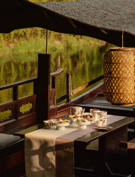Afternoon tea service on wooden table at Amanyangyun, with views of golden-hued landscape through open-sided pavilion.