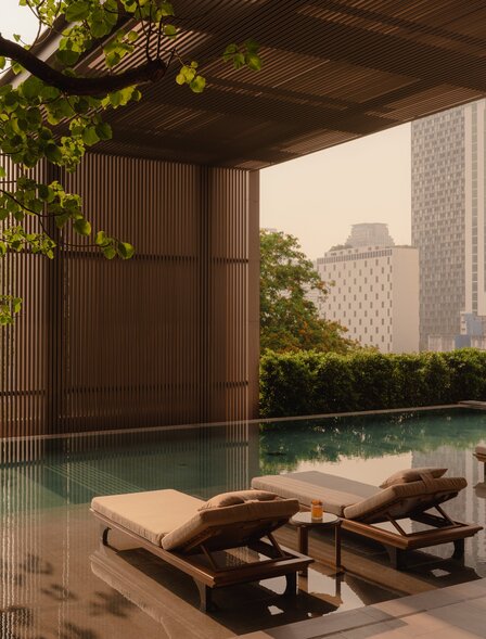 Swimming pool at Aman Nai Lert Bangkok, framed by wooden pavilion with climbing greenery.