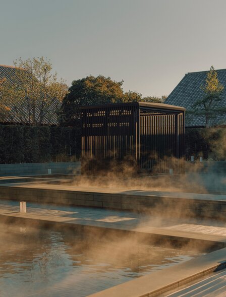 Wooden spa pavilion beside steaming onsen pool at Amanemu resort, Japan.