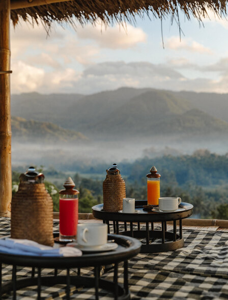 Sunrise breakfast at Amankila with coloured bottles and traditional setup overlooking misty Balinese mountains.