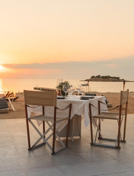Dining table and chairs set on a terrace at Amanzoe at sunset, overlooking the Aegean Sea.