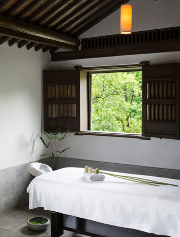 Amanfayun bathroom with wooden window frame overlooking village greenery, white bathtub, and pendant lighting.