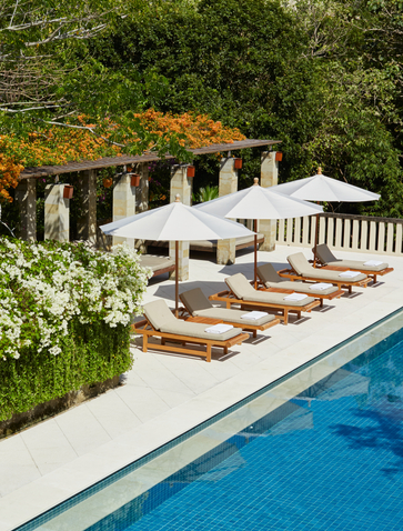 Villa pool at Aman Villas at Nusa Dua with loungers and pergola beside turquoise water.