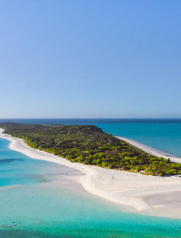 Aerial view of Pamalican Island at Amanpulo, showing white-sand beach, turquoise waters, and forested interior.